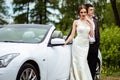 Gorgeous bride with fashion makeup and hairstyle in a luxury wedding dress with handsome groom near white cabriolet car Royalty Free Stock Photo