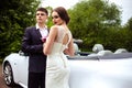 Gorgeous bride with fashion makeup and hairstyle in a luxury wedding dress with handsome groom near white cabriolet car Royalty Free Stock Photo