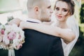 Gorgeous bride gently hugging groom and holding wedding bouquet in sunset light. Beautiful stylish wedding couple embracing in Royalty Free Stock Photo
