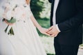 Gorgeous bride and groom gently holding hands in evening park. Stylish wedding couple embracing, holding hands during walk in Royalty Free Stock Photo