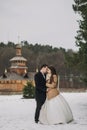 Gorgeous bride and groom walking at wooden church in autumn forest. happy newlywed couple hugging in woods after holy wedding Royalty Free Stock Photo