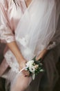 Gorgeous bride holding boutonniere, sitting in robe near window. beautiful woman getting ready for wedding day, holding flowers. Royalty Free Stock Photo