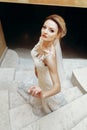 Gorgeous bride in sexy white wedding dress posing on marble staircase indoors, beautiful blonde bride portrait on stairs in Royalty Free Stock Photo