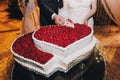 Gorgeous bride and stylish groom cutting together delicious wedding cake in two hearts shape with fresh strawberries at wedding Royalty Free Stock Photo