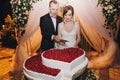 Gorgeous bride and stylish groom cutting together delicious wedding cake in two hearts shape with fresh strawberries at wedding Royalty Free Stock Photo