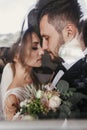 Gorgeous bride and stylish groom gently hugging at window. Sensual wedding couple embracing. Romantic moments of newlyweds.