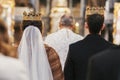 Gorgeous bride and stylish groom in golden crowns, standing with priest in church during wedding ceremony. spiritual newlywed