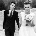 Gorgeous bride and stylish groom holding hands and looking at sandy beach lake, black and white photo, luxury wedding Royalty Free Stock Photo