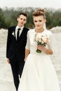 Gorgeous bride and stylish groom holding hands and looking at sandy beach lake, true emotions, luxury wedding Royalty Free Stock Photo