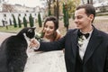 Gorgeous bride and stylish groom  playing with cute black and white cat in european city street in autumn. happy wedding couple Royalty Free Stock Photo