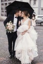 Gorgeous bride and stylish groom walking under umbrella in rainy Royalty Free Stock Photo