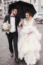 Gorgeous bride and stylish groom walking under umbrella in rainy Royalty Free Stock Photo