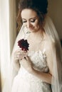 Gorgeous bride in vintage lace white wedding dress holding red flower, portait of beautiful woman posing near a window, wedding Royalty Free Stock Photo