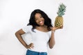 Gorgeous charming lovely young african girl with curly hair, in a white t-shirt and jeans, holding a pineapple in hands