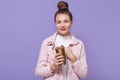 Gorgeous charming young female with hair knot holding large thermo mug, enjoying freshly made coffee, wearing white shirt and