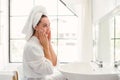 Gorgeous confident adult woman wearing a towel on her head sitting and checking her face in front of the mirror. Royalty Free Stock Photo