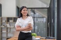Gorgeous and confident Asian businesswoman or female manager in formal suit standing at her desk, holding a coffee cup Royalty Free Stock Photo