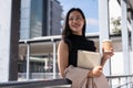 A gorgeous Asian businesswoman with her digital tablet and a coffee cup is standing on a skywalk Royalty Free Stock Photo