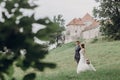 Gorgeous couple of newlyweds holding hands outdoors surrounded by nature, groom and bride on a walk near old castle, wedding Royalty Free Stock Photo