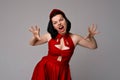 Gorgeous emotional dark-haired young woman in red dress, standing over gray background