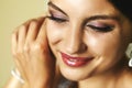 Gorgeous emotional smiling exotic bride putting on earrings closeup