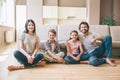 Gorgeous family are sitting on the floor with their legs grossed and looking on camera. They smile. Guy is leaning to