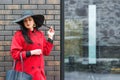 Gorgeous fashionable woman walking on the street. Girl wearing stylish red coat and black fashion hat. Fashion, beauty, makeup. Royalty Free Stock Photo
