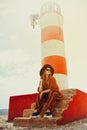 Gorgeous fashionable woman posing while sitting on a lighthouse. Summer photo of a girl in a yellow-orange suit, black hat and