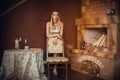 A gorgeous girl with bright make-up, with blond hair, in a dress, stands in a room with a fireplace, near the table Royalty Free Stock Photo