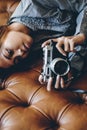Gorgeous girl lying on leather sofa with photo camera in her hands