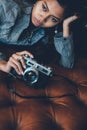 Gorgeous girl lying on leather sofa with photo camera in her hands