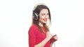 Gorgeous girl in red swaying along with the music in big headphones noticing camera and shying isolated on white background