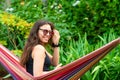 Gorgeous girl with sunglasses sitting on a hammock, relaxing and using a smartphone Royalty Free Stock Photo