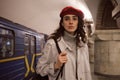 Gorgeous girl in trench coat and red beret thoughtfully waiting train at subway station Royalty Free Stock Photo