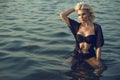 Gorgeous glam tanned blond woman wearing trendy black two piece strapless swimsuit and summer tunic sitting in the transparent sea