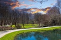 A gorgeous green pond in the garden surrounded by lush green grass, smooth footpaths, bare winter trees, lush green trees Royalty Free Stock Photo