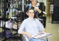 Gorgeous happy woman looking to the camera while examining hair dye color chart with her hairdresser at the beauty salon treatment