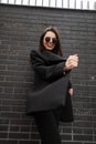 Gorgeous happy young woman with beautiful joyful smile in trendy round sunglasses in cool black youth clothes posing near brick Royalty Free Stock Photo