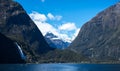 Gorgeous image of Milford Sound with a waterfall in the foreground and snow capped mountains in the background taken on a sunny