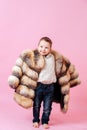 Gorgeous imaginative boy posing in oversize luxurious fur coat. Over dark pink