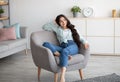 Gorgeous Indian woman sitting in comfy armchair, enjoying lazy morning, having peaceful weekend at home Royalty Free Stock Photo