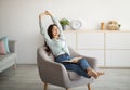 Gorgeous Indian woman stretching in comfy armchair while reading indoors Royalty Free Stock Photo