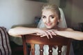 Gorgeous innocent blonde bride posing while sitting on wooden ch Royalty Free Stock Photo