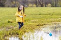 Gorgeous little girl holding paper ship and looking at camera with shiny smile, preparing to launch boat on puddle. Royalty Free Stock Photo