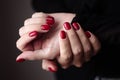 Gorgeous manicure, clssic red color nail polish, closeup photo. Female hands over dark background