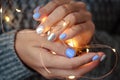 Gorgeous manicure, pastel tender color nail polish, closeup photo. Female hands hold a christmas light garland