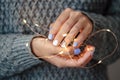 Gorgeous manicure, pastel tender color nail polish, closeup photo. Female hands hold a christmas light garland