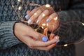 Gorgeous manicure, pastel tender color nail polish, closeup photo. Female hands hold a christmas light garland