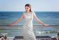 A gorgeous model woman in a white dress with patterns on a background of the sea. The lady with dark hair is on summer vacation.