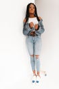 Gorgeous modern African American woman in trendy top in sexy stylish blue jeans in shoes with cool long dreadlocks stands near